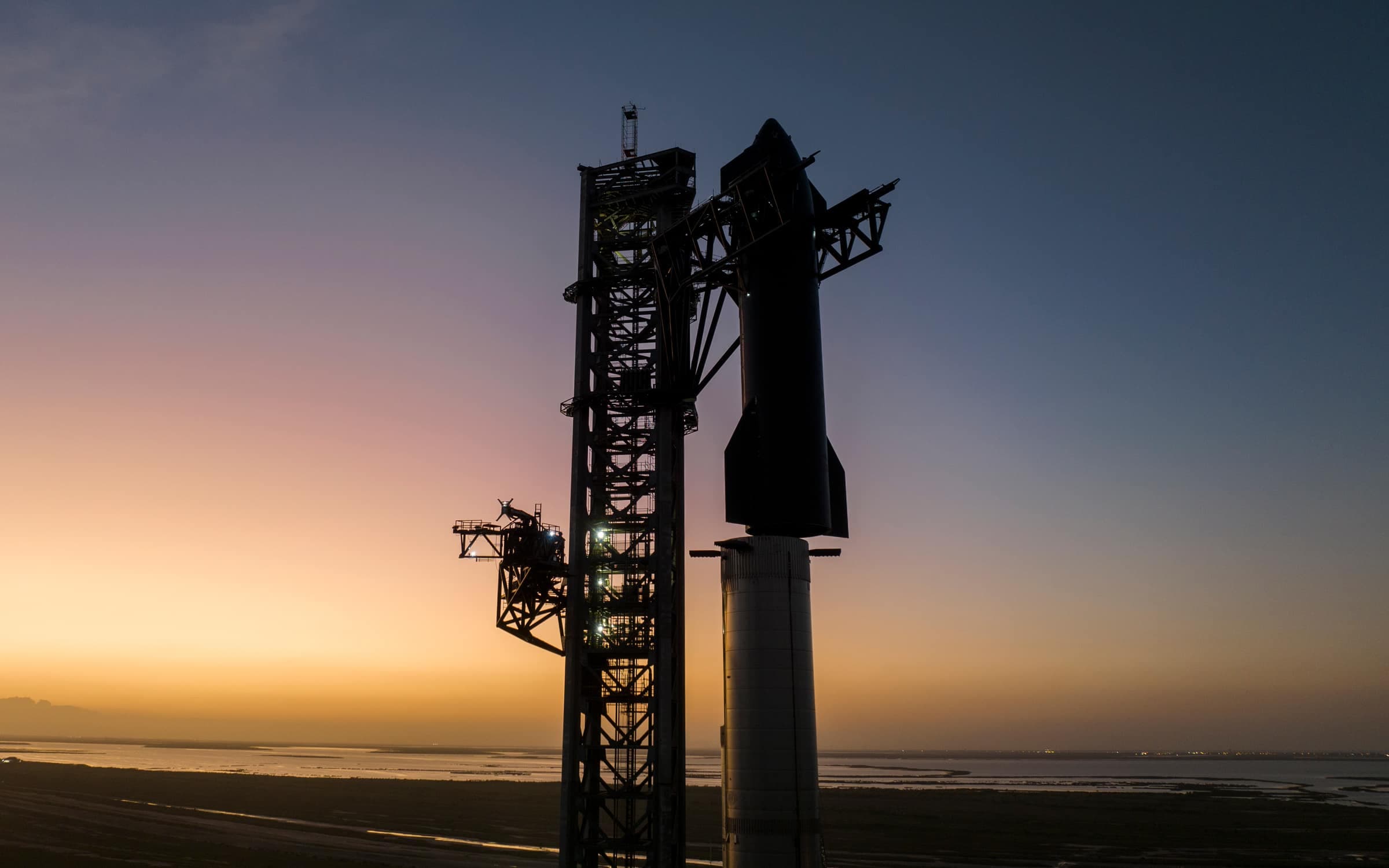A Starship and its launch tower in silhouette against a sunset sky at Starbase, Texas