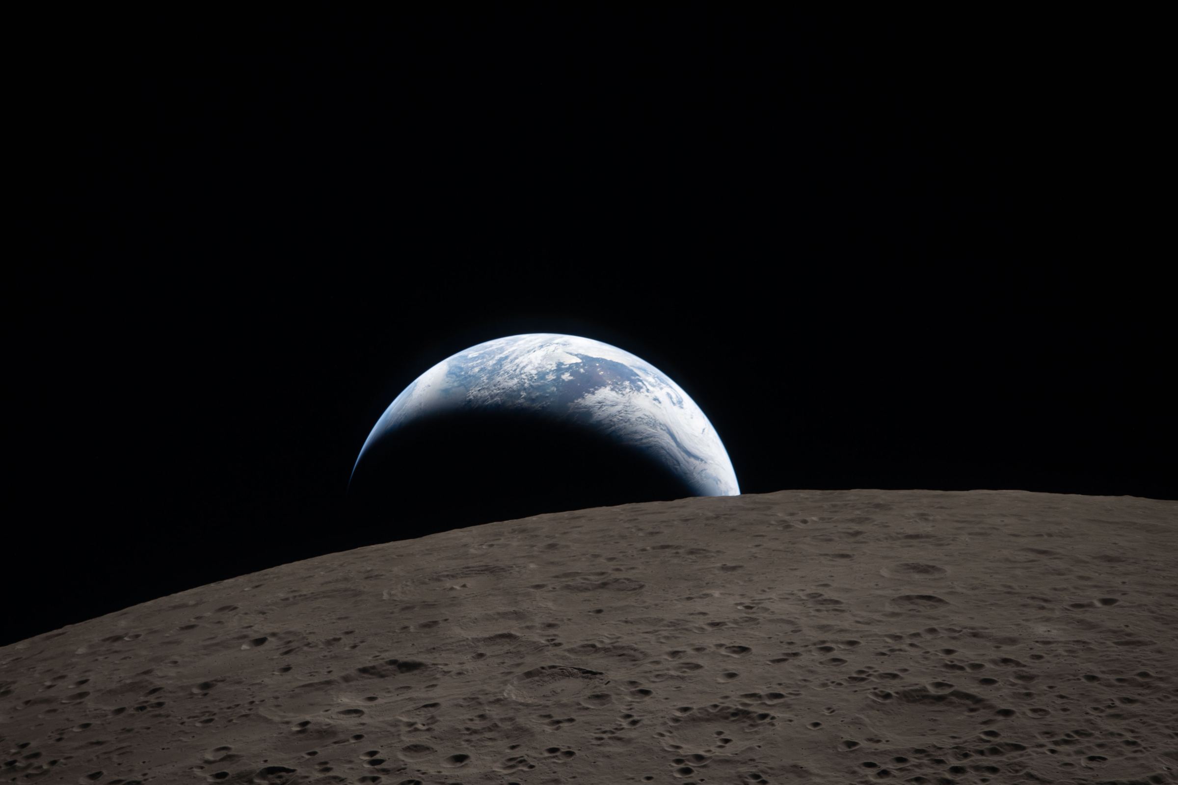 A crescent Earth rising over the cratered horizon of the Moon